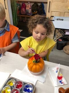Coronation Montessori girl in yellow painting a pumpkin